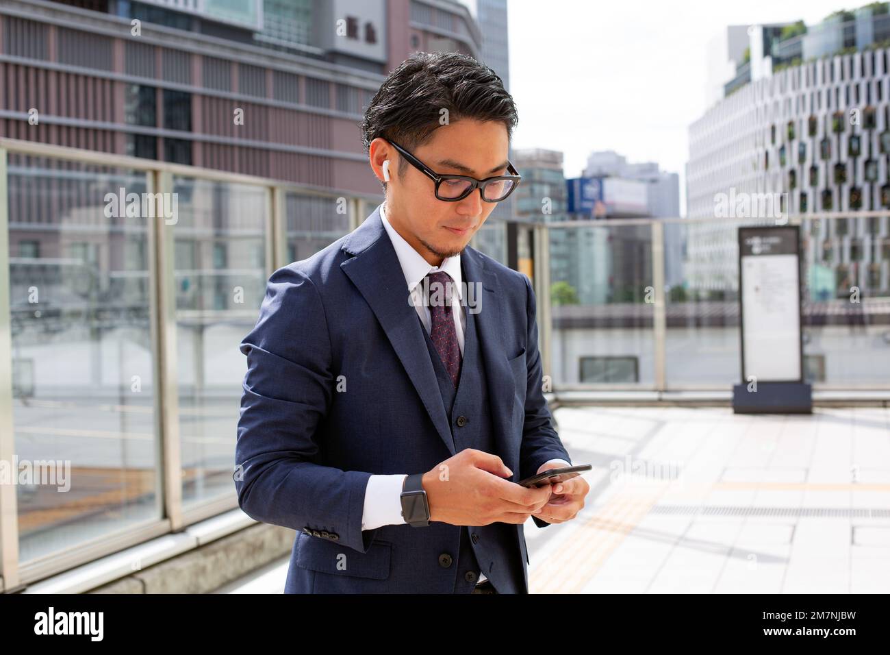 Ein junger Geschäftsmann in der Stadt, der unterwegs ist, ein Mann draußen im Anzug, der auf sein Handy schaut. Stockfoto