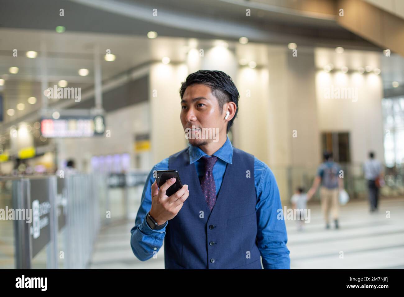 Ein junger Geschäftsmann in der Stadt, der unterwegs ist, an einem Verkehrsknotenpunkt, sein Handy in der Hand hält und sich umsieht. Stockfoto