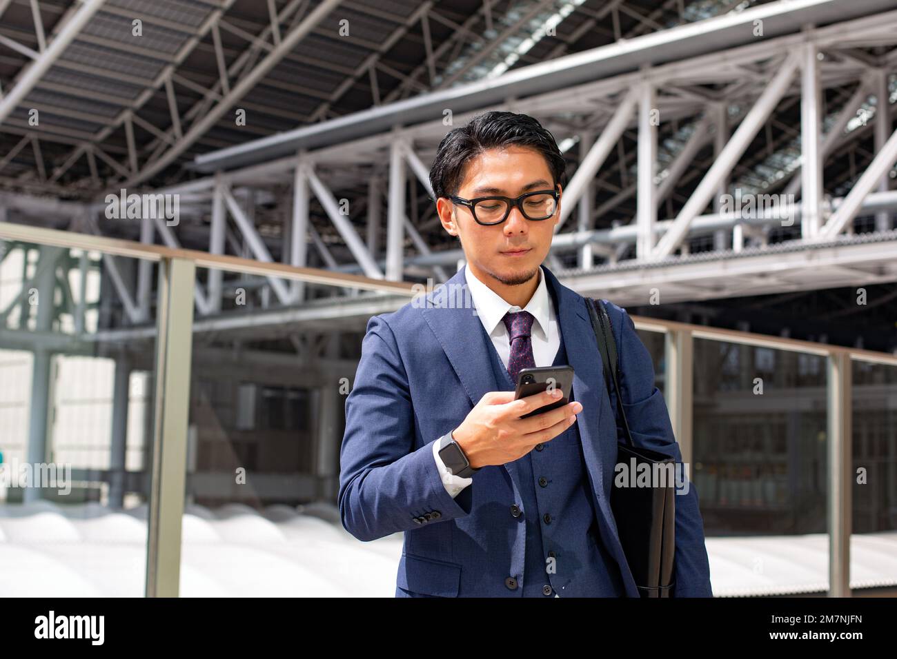 Ein junger Geschäftsmann in der Stadt, der unterwegs ist, ein Mann in einem blauen Anzug mit einer Laptop-Tasche, der ein Handy in der Hand hat. Stockfoto
