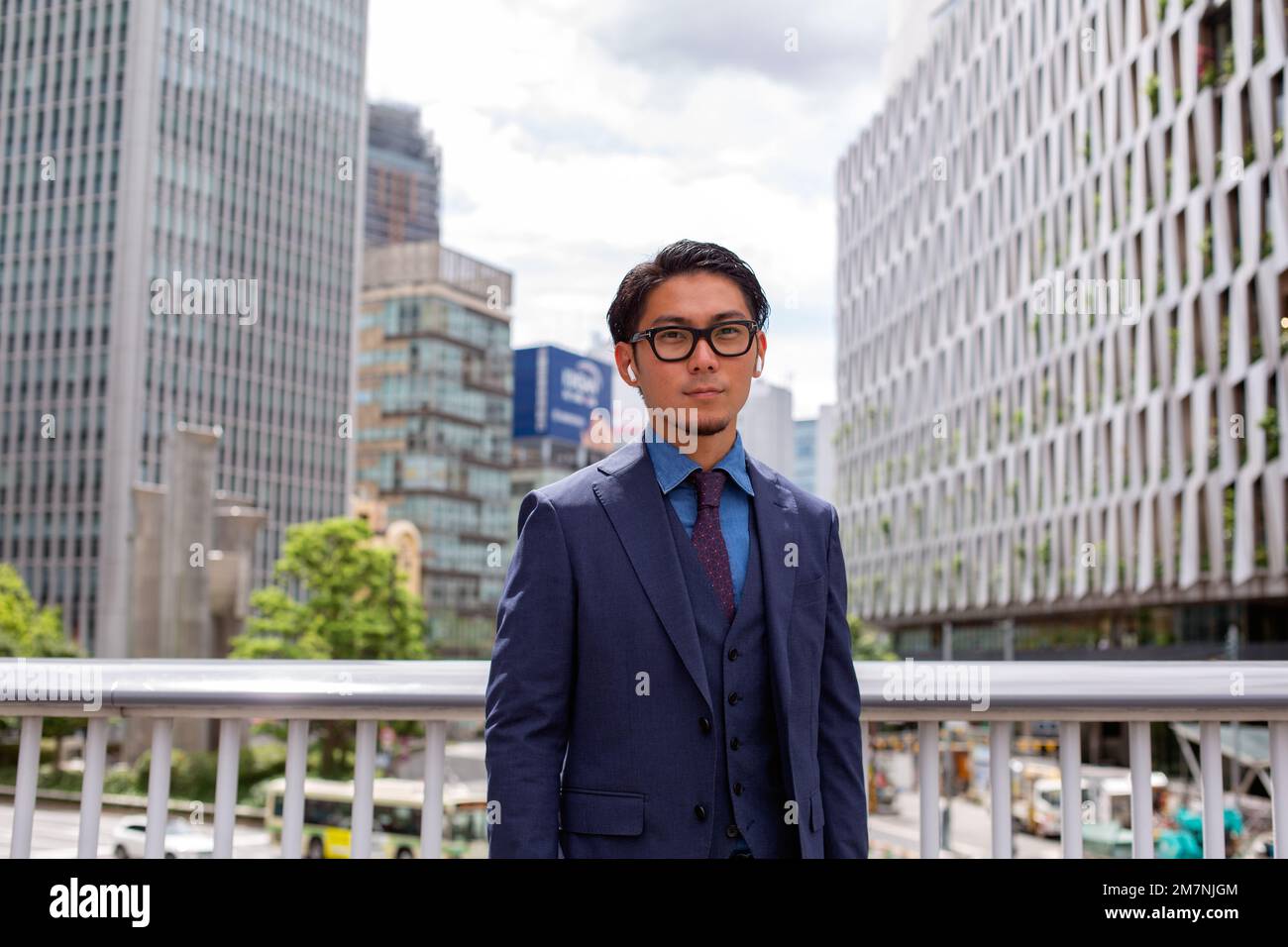 Ein junger Geschäftsmann in blauer Jacke, Hemd und Krawatte, der auf einem Fußweg in der Innenstadt steht. Stockfoto