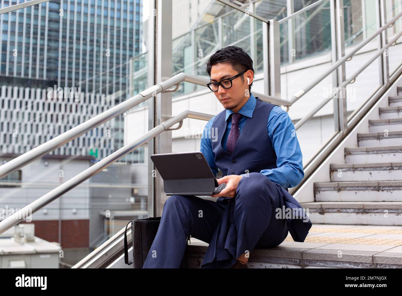 Ein junger Geschäftsmann in der Stadt, der unterwegs ist, auf der Treppe am Fenster sitzt und einen Laptop benutzt. Stockfoto
