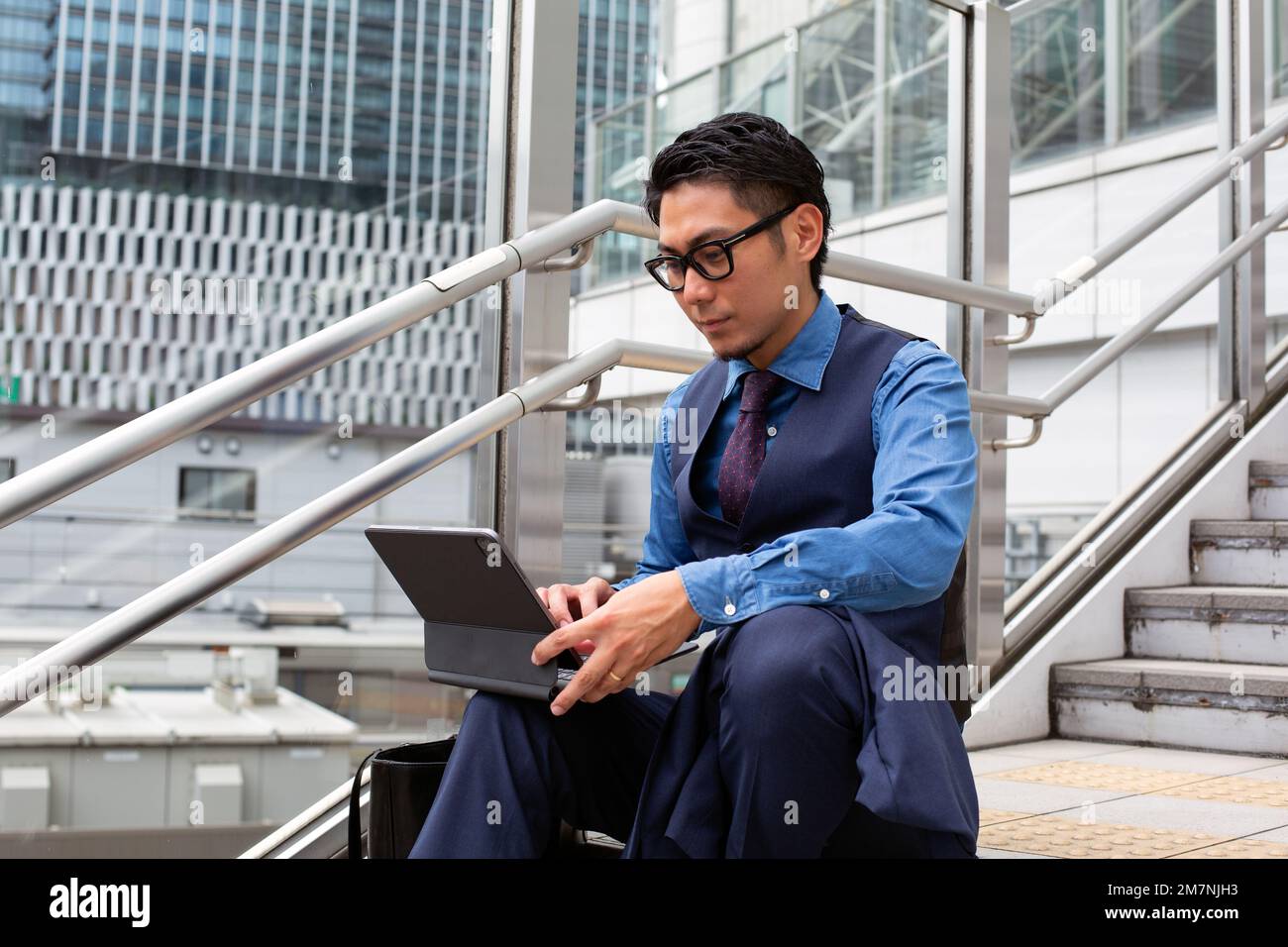 Ein junger Geschäftsmann in der Stadt, der unterwegs ist, auf der Treppe am Fenster sitzt und einen Laptop benutzt. Stockfoto