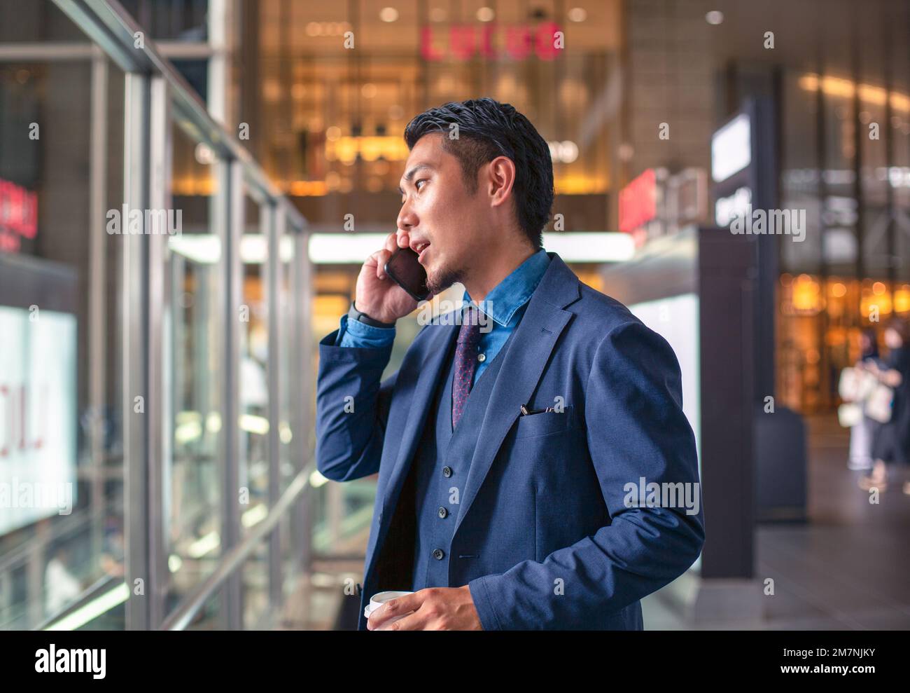 Ein junger Geschäftsmann in einem blauen Anzug, der in der Innenstadt unterwegs ist und mit seinem Handy spricht. Stockfoto