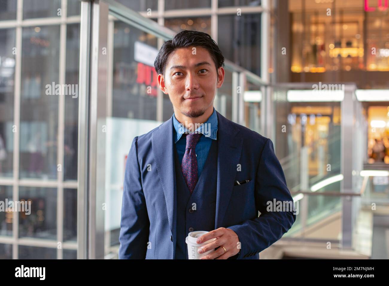 Ein junger Geschäftsmann im blauen Anzug, der in der Innenstadt unterwegs ist und eine Tasse Kaffee mit sich führt. Stockfoto