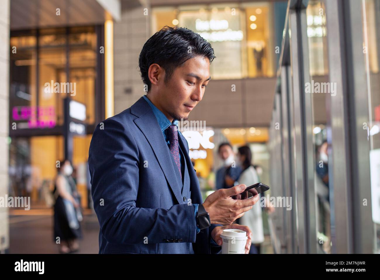 Ein junger Geschäftsmann in einem blauen Anzug in einer Stadt, der auf sein Handy schaut, eine SMS schreibt oder eine Nachricht liest. Stockfoto