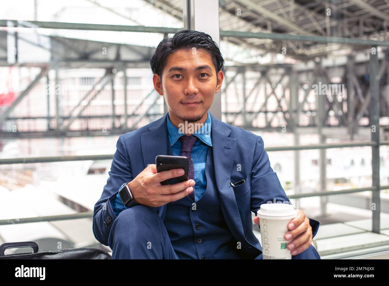Ein junger Geschäftsmann in einem blauen Anzug in einer Stadt, der auf sein Handy schaut, eine SMS schreibt oder eine Nachricht liest. Stockfoto
