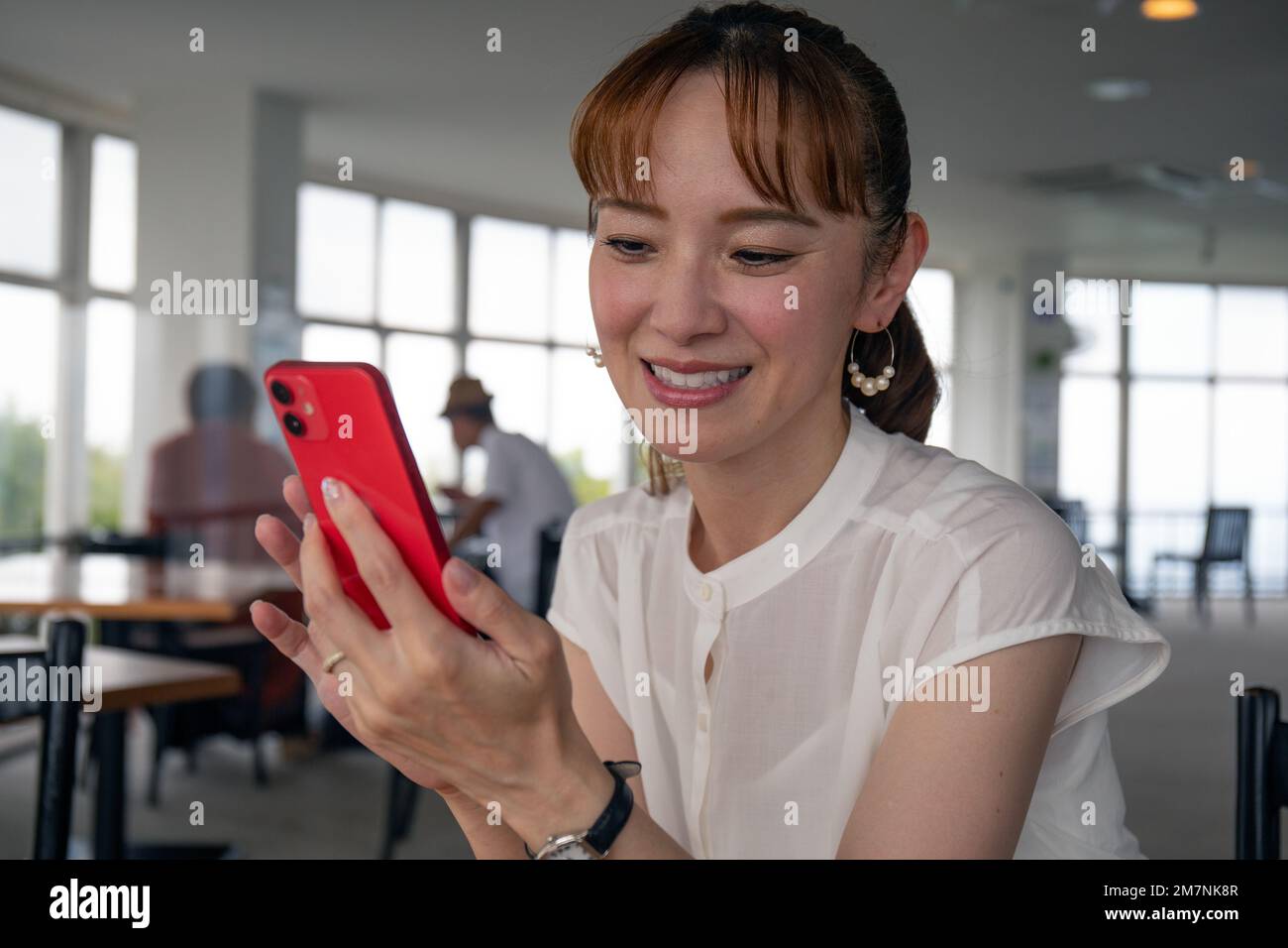 Eine reife japanische Frau, die auf ihren Telefonbildschirm schaut und lächelt, eine SMS sendet, Nachrichten sendet. Stockfoto