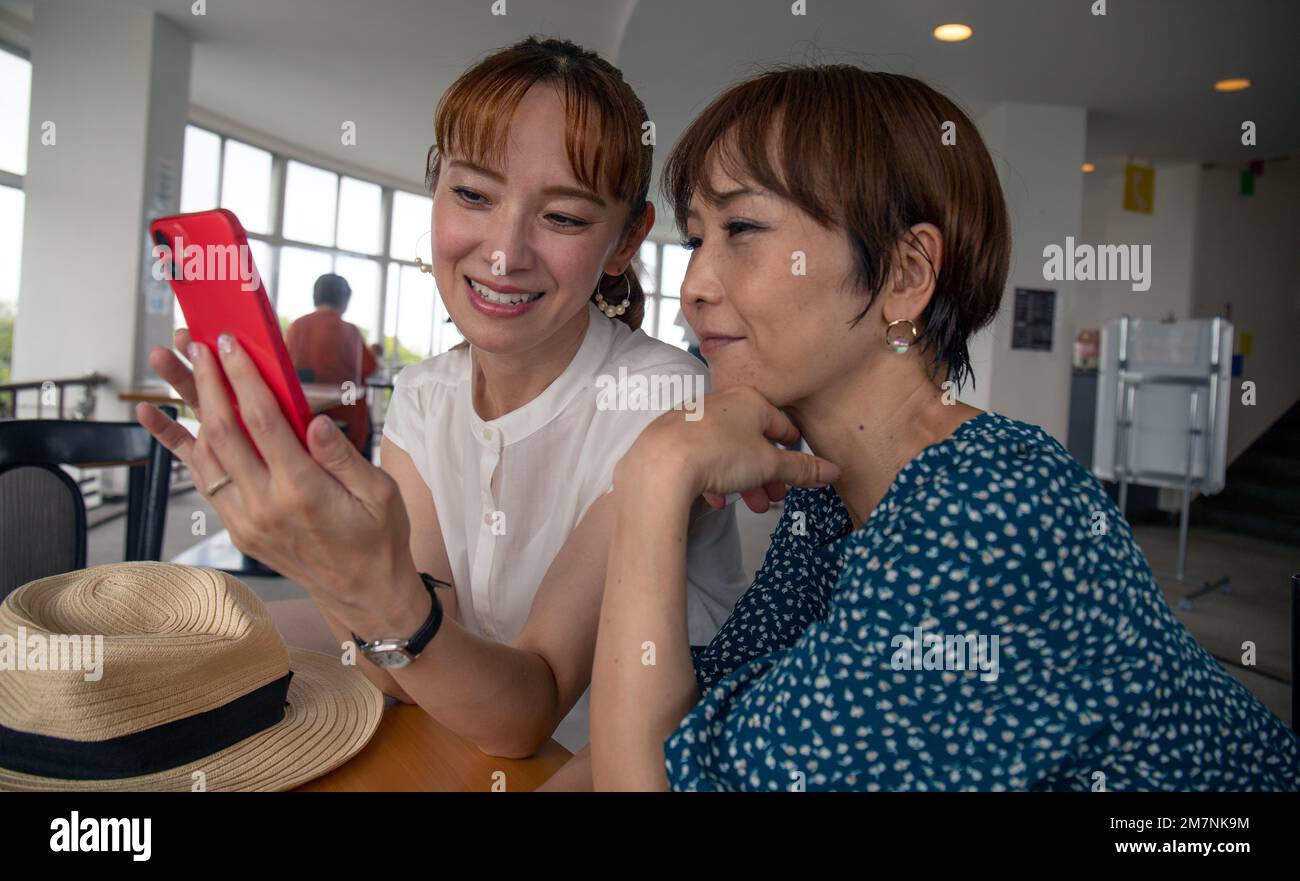 Zwei reife japanische Frauen, Freunde Seite an Seite, die auf den Bildschirm eines Mobiltelefons schauen. Stockfoto