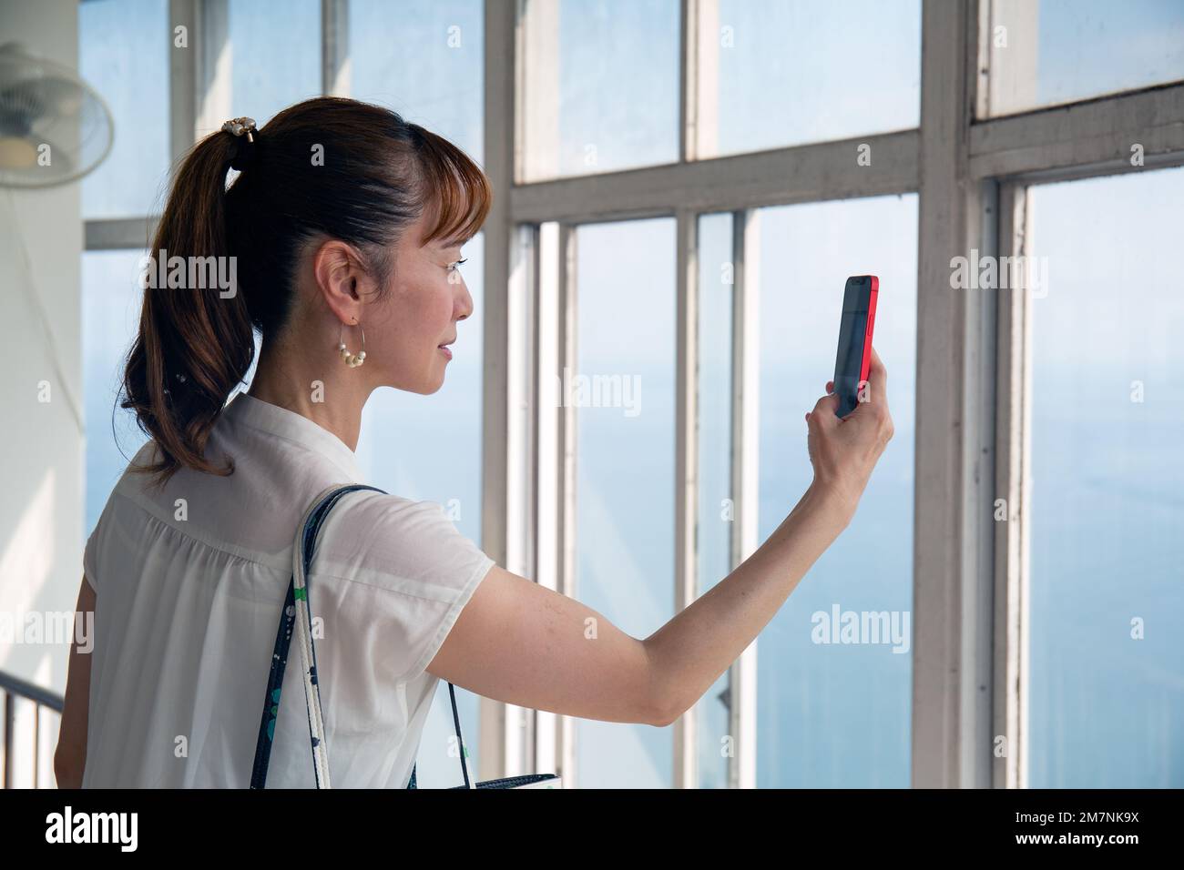 Eine reife japanische Frau, die mit ihrem Mobiltelefon Fotos von einer Aussichtsplattform der Stadt und der Landschaft darunter machte. Stockfoto