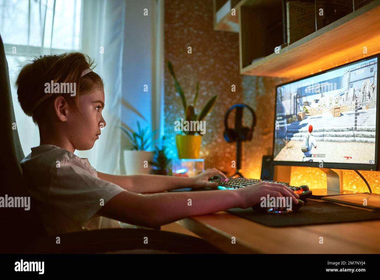 Bild von eingetaucht teenage Gamer junge Videospiele auf Computer im dunklen Zimmer Kopfhörer tragen und mit bunten Tastatur mit Hintergrundbeleuchtung Stockfoto