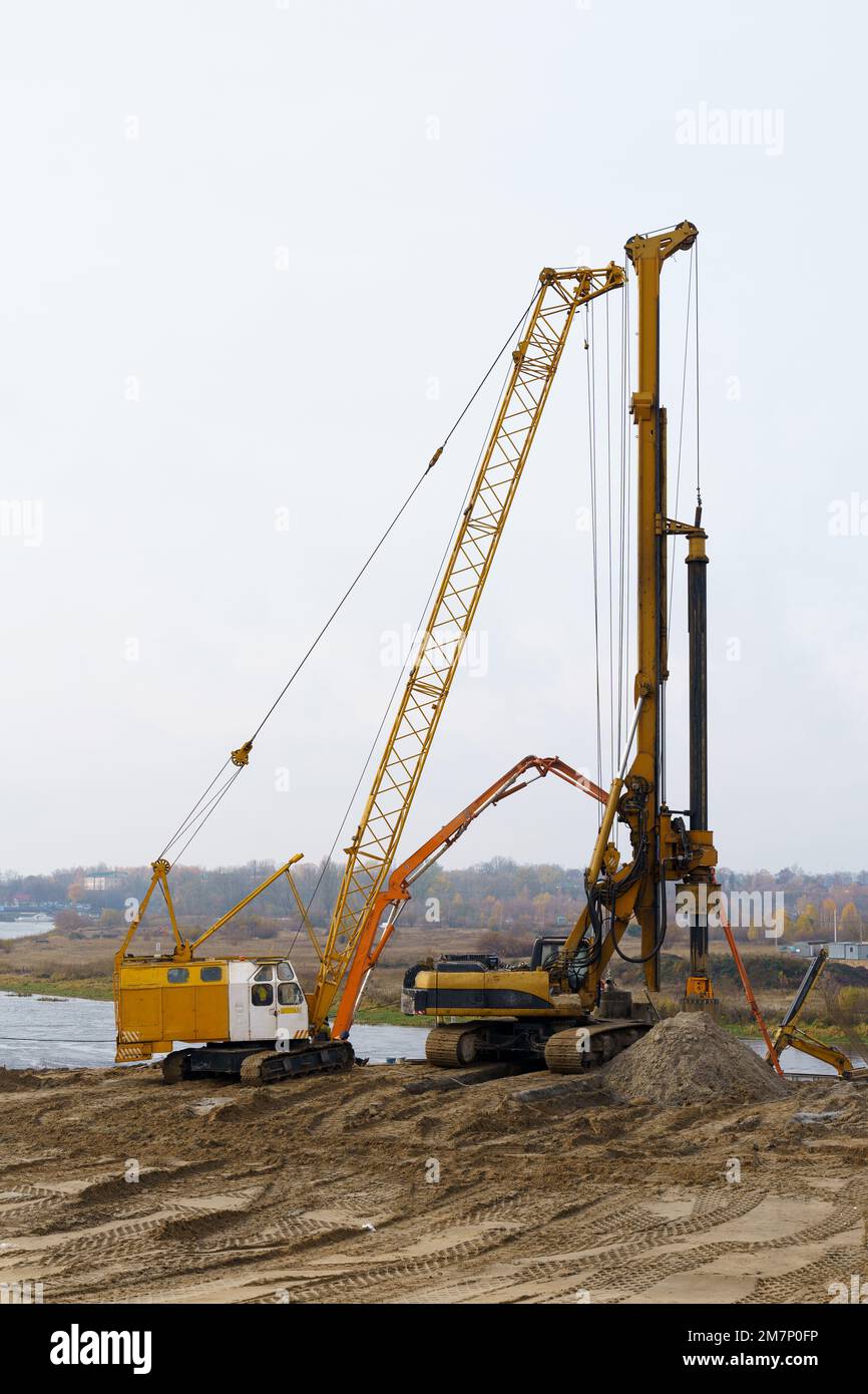 Die Arbeit von Kranen und anderen Geräten auf der Baustelle der Brücke über den Fluss. Stockfoto