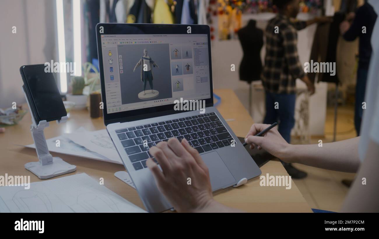 Modedesignerin entwickelt zukünftiges Design von Kleidung im 3D-Modellierungsprogramm auf einem Laptop mit digitalem Tablet und Eingabestift. Sie arbeitet in einer Atelier-Werkstatt. Mode und Technik im Geschäftskonzept. Stockfoto