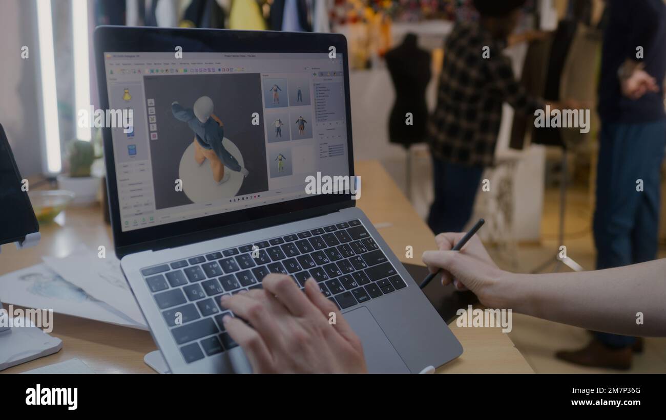 Modedesignerin entwickelt zukünftiges Design von Kleidung im 3D-Modellierungsprogramm auf einem Laptop mit digitalem Tablet und Eingabestift. Sie arbeitet in einer Atelier-Werkstatt. Mode und Technik im Geschäftskonzept. Stockfoto