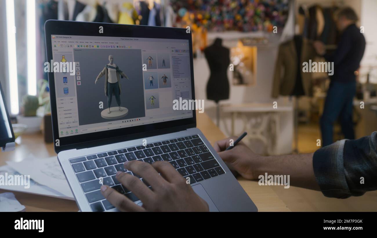 Afroamerikanischer Modedesigner kreiert Kleidung in 3D-Modelliersoftware auf einem Laptop mit digitalem Tablet und Eingabestift. Er arbeitet in der Atelier-Werkstatt. Mode- und Technologiekonzept in der Wirtschaft. Stockfoto
