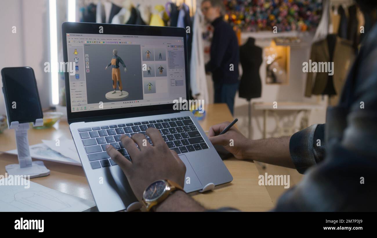 Afroamerikanischer Modedesigner kreiert Kleidung in 3D-Modelliersoftware auf einem Laptop mit digitalem Tablet und Eingabestift. Er arbeitet in der Atelier-Werkstatt. Mode- und Technologiekonzept in der Wirtschaft. Stockfoto