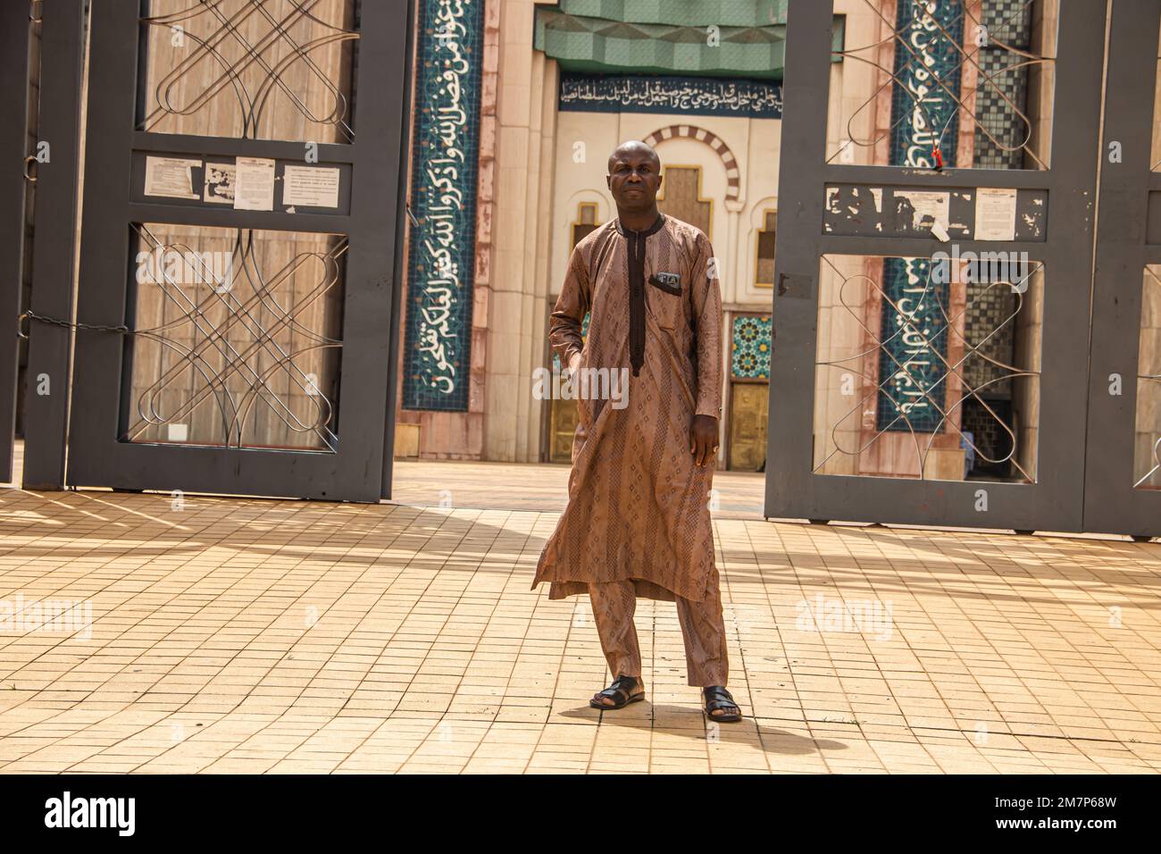 Traditionell gekleidete Person, die eine Fassade der wunderschönen Moschee in Abuja, Nigeria, präsentiert. Die Nationalmoschee von Abuja ist die Nationalmoschee von Nigeria. Stockfoto