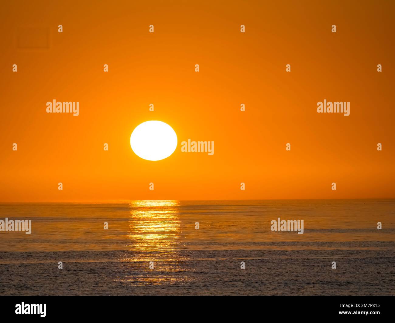 Die Sonne geht in einem leeren orangefarbenen Himmel über dem Horizont über dem Golf von Mexiko unter Stockfoto