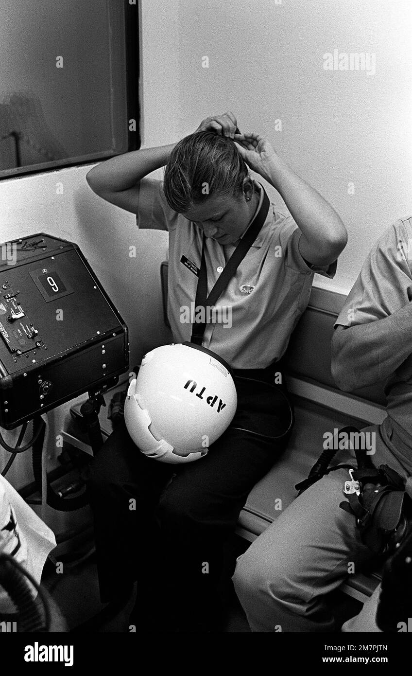 Eine Fähnrich-Frau bindet ihr Haar fest, bevor sie einen Helm für ihren simulierten „Flug“ in einer Überdruckkammer der Aviation Physiology Training Unit aufsetzt. Sie nimmt an einem einwöchigen Flugschulungsprogramm für Studenten des Naval Reserve Officers Training Corps (NROTC) Teil. Basis: Marineflugstation, Miramar Bundesstaat: Kalifornien (CA) Land: Vereinigte Staaten von Amerika (USA) Stockfoto