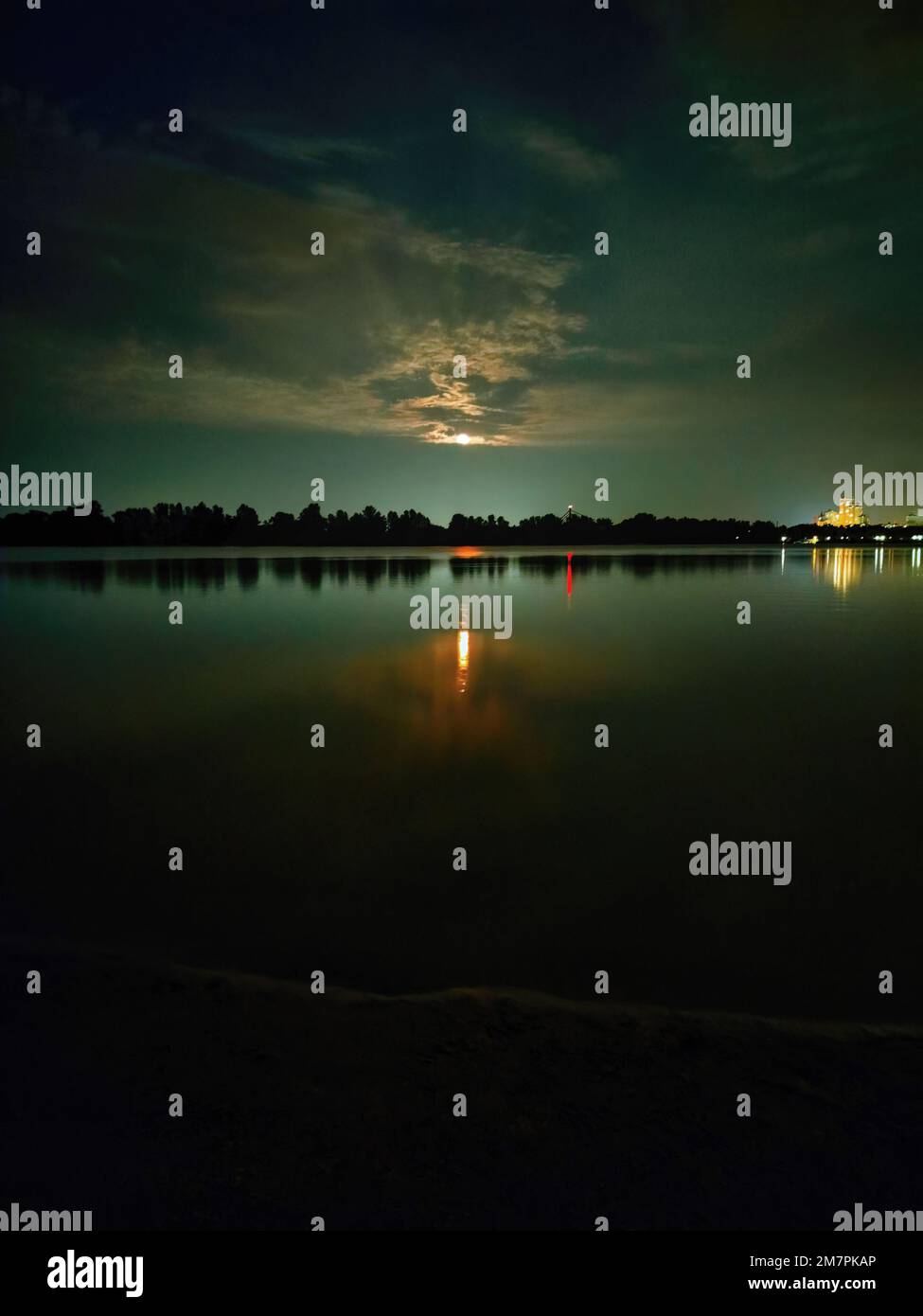 Farbfotografie der abendlichen Natur am Fluss. Aufsteigender Vollmond über den Bäumen. Wunderschöne Reflexion des Mondwegs im Wasser. Stockfoto