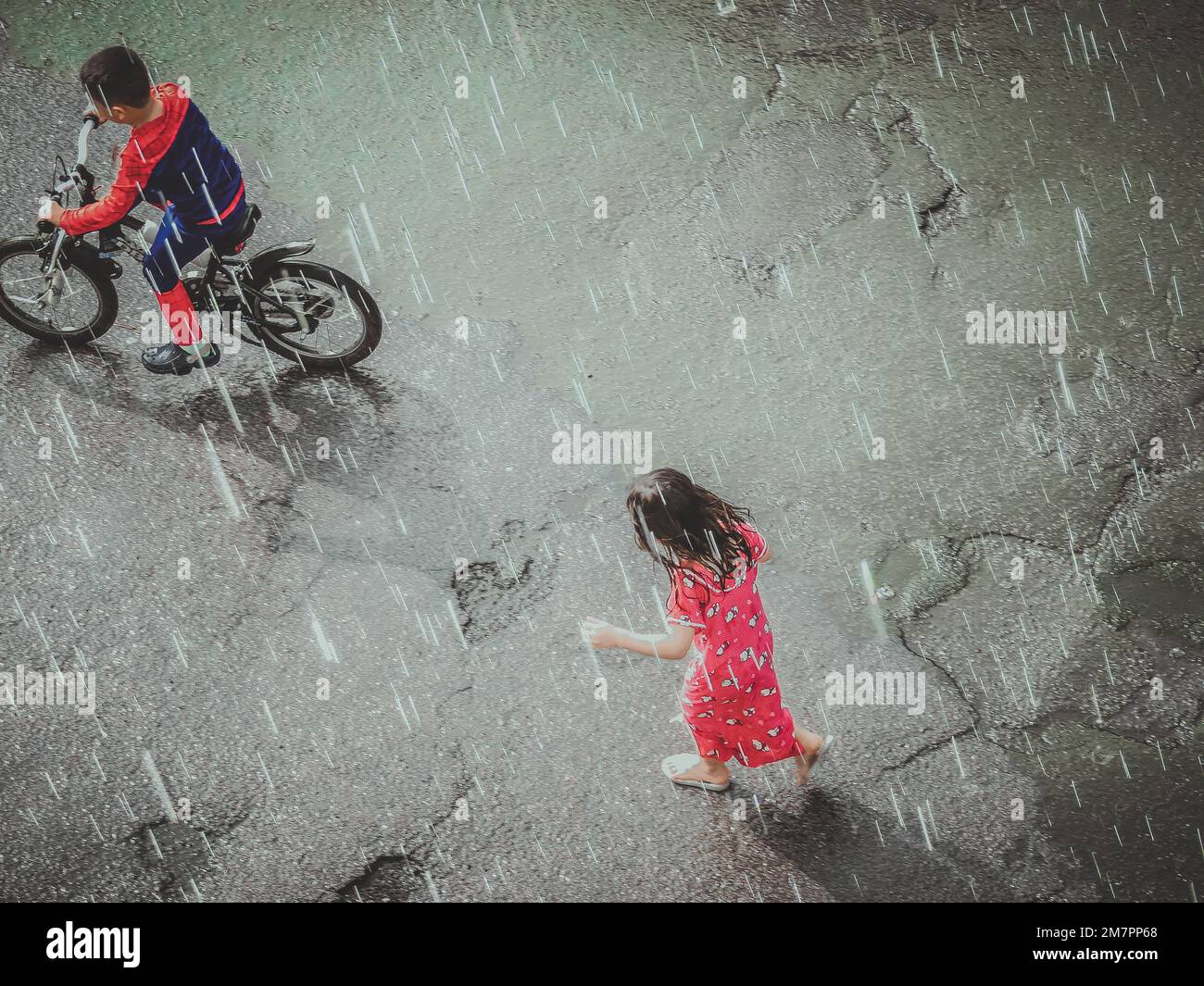 Ein Luftbild eines Jungen auf einem Fahrrad und eines Mädchens im Rock, das unter dem Regen rennt Stockfoto