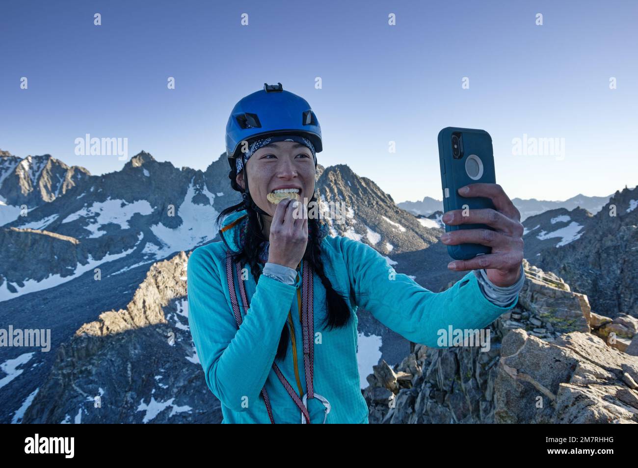 Eine Klettererin aus Asien mit Helm macht ein Gipfelkeks-Selfie auf dem Two Eagle Peak im Palisade Basin der Sierra Nevada Stockfoto