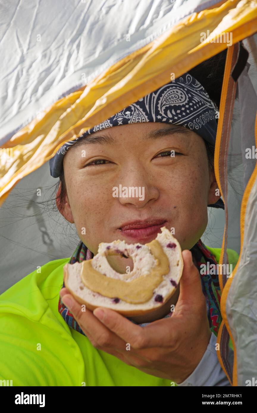 Porträt einer Asiatin in einem Zelt, die einen Bagel mit Erdnussbutter isst Stockfoto
