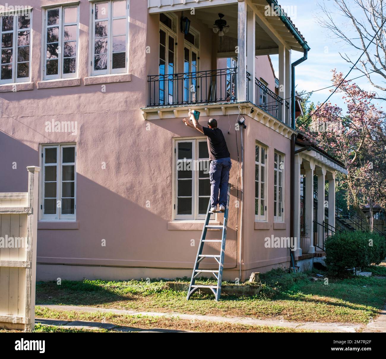 NEW ORLEANS, LA, USA - 9. DEZEMBER 2022: Arbeiter auf einer Leiter malt die Seite eines rosafarbenen Hauses im Viertel Carrollton Stockfoto