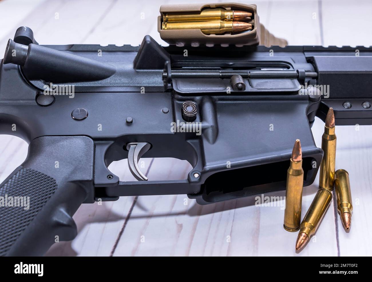 Ein AR15-Gewehr in Kaliber 223 mit vier Kugeln und ein geladenes Magazin daneben auf weißem Holzhintergrund. Stockfoto