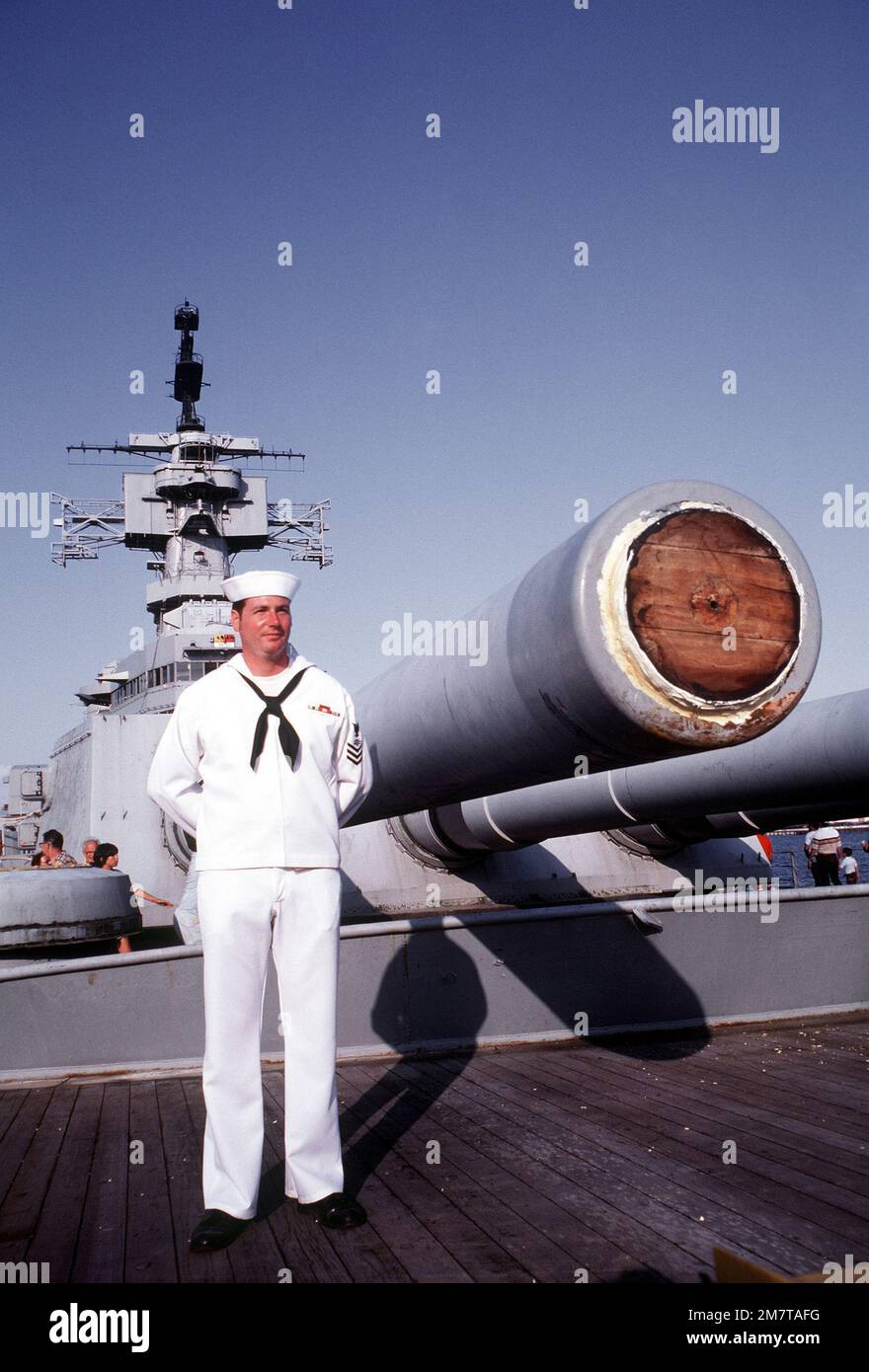 Ein Crewman in weißer Uniform steht in der Nähe von Mark 7 16 Zoll/50 Kaliber Gewehren auf dem vorderen Deck des Schlachtschiff USS NEW JERSEY (BB-62). Das Schiff wurde kürzlich wegen Umrüstung und Reaktivierung hierher abgeschleppt. Basis: Long Beach Bundesstaat: Kalifornien (CA) Land: Vereinigte Staaten von Amerika (USA) Stockfoto