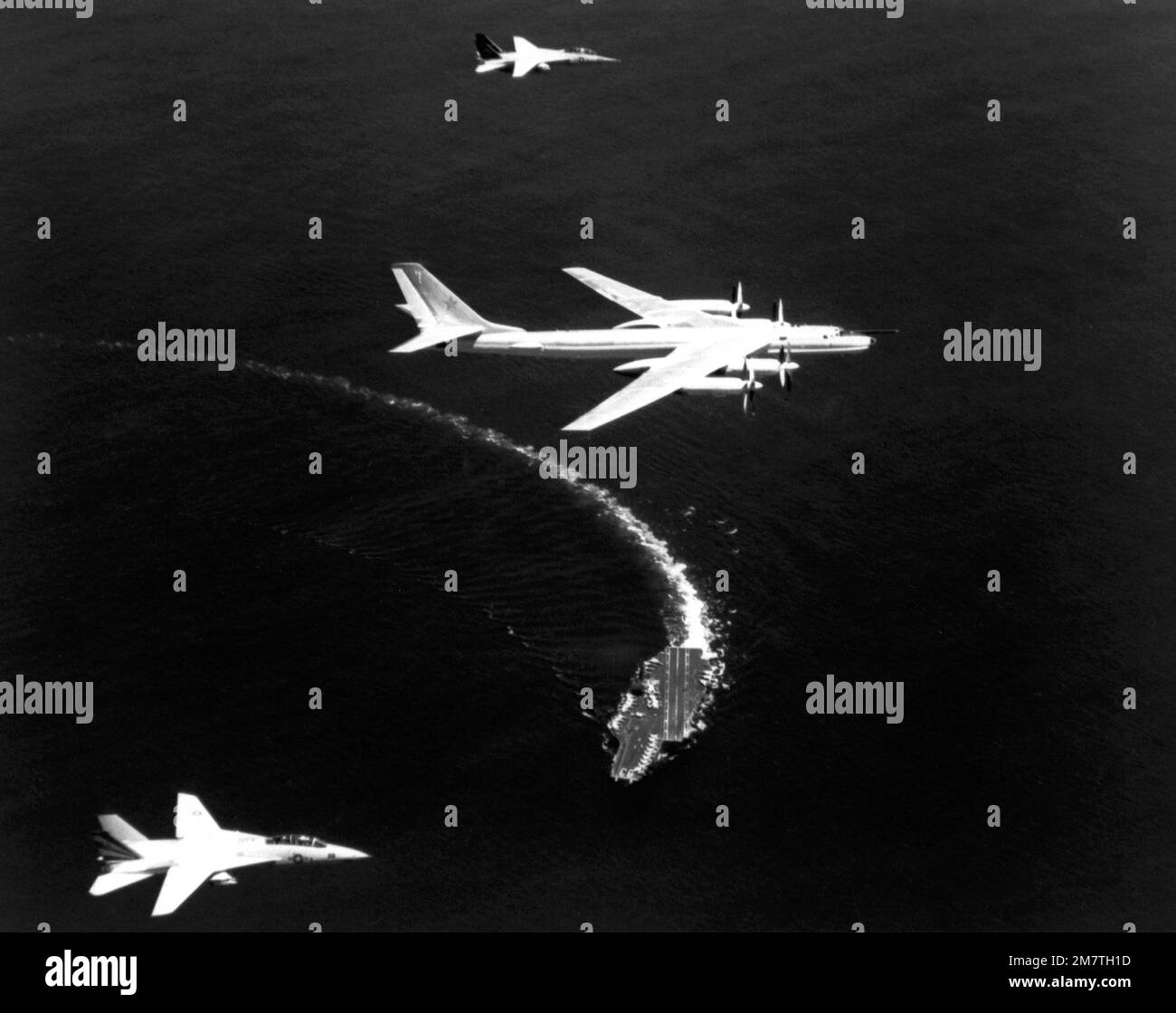 Eine Air-to-Air-Ansicht von rechts eines russischen TU-95 Tupolev Bomberflugzeugs, Center, und zwei US-Flugzeuge Navy F-14 Tomcat-Flugzeug, das als Verfolgungsflugzeuge über dem Flugzeugträger USS KITTY HAWK (CV-63) fungiert, während das Schiff nach rechts abbiegt. Die NATO-Bezeichnung des Tupolev-Flugzeugs ist Bear. Land: Unbekannt Stockfoto