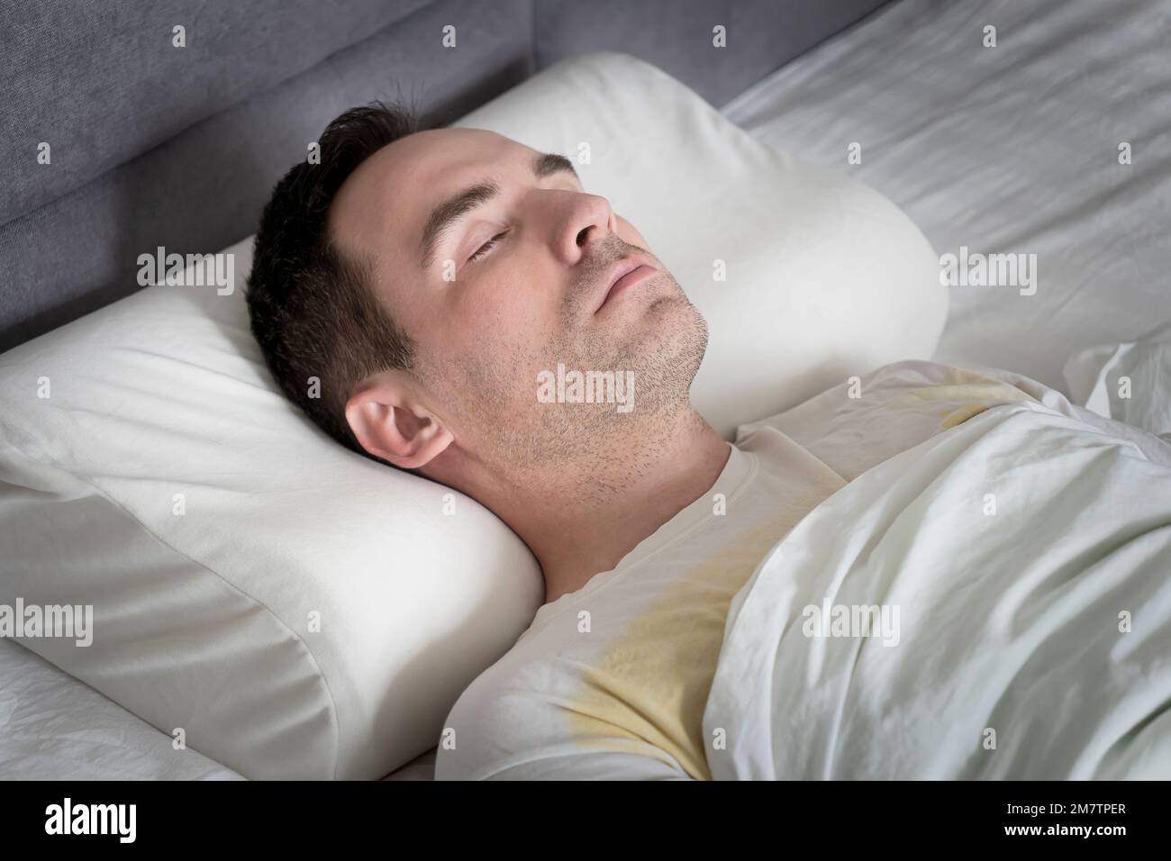 Süßer junger Mann, der auf einem orthopädischen Kissen im Bett schläft Stockfoto