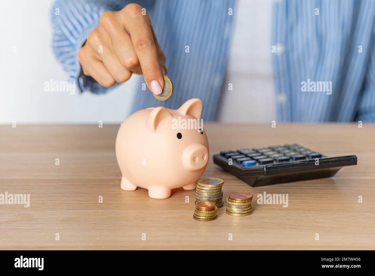Nahaufnahme der Hände einer Frau Legen Sie eine Euro-Münze in ein  Sparschwein, neben einem Rechner auf den Tisch.richtige Investition. Geld  sparen in Zeiten der Krise und Stockfotografie - Alamy