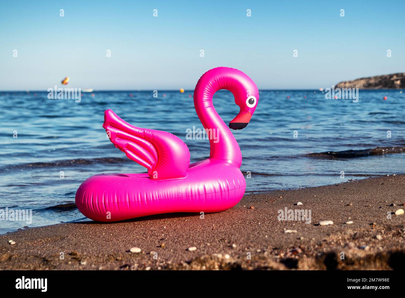 Aufblasbarer rosa Flamingo am Sandstrand mit Meer im Hintergrund. Stockfoto