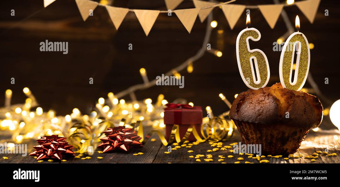Nummer 60 goldene festliche brennende Kerzen in einem Kuchen, hölzerner Feiertagshintergrund. 60 