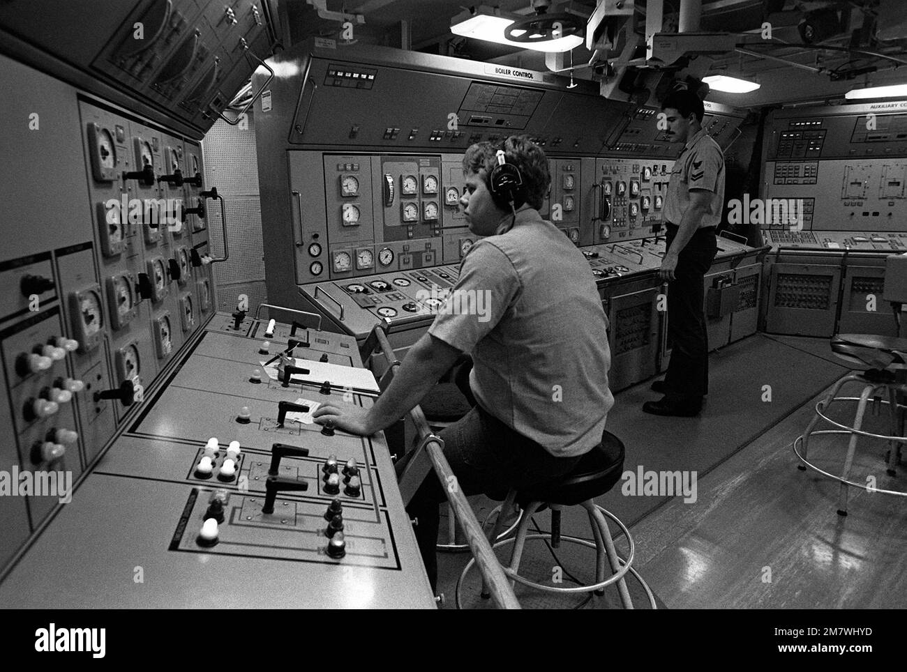 Mate 2., Klasse Melvin Johnson, steht, überwacht das automatische Verbrennungssteuerungssystem im Maschinenraum an Bord des Fleet-Ölers USS CIMARRON (AO-177), während ein Innenraum-Kommunikationstechniker die elektrische Konsole managt. Basis: USS Cimarron Stockfoto