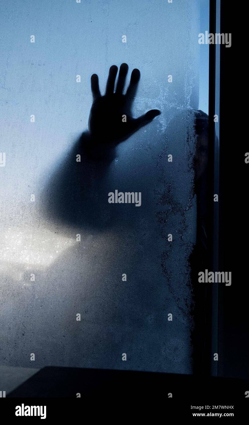 Schattige Figur vor einer Glastür mit der Hand auf dem frostigen Glas, Thriller-Buchumschlag. Stockfoto