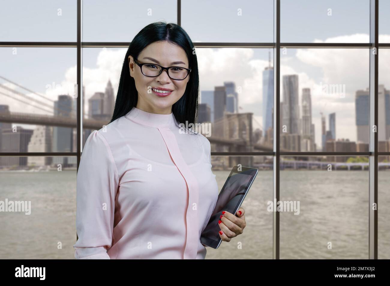 Porträt einer klugen, glücklichen asiatischen Frau mit Tablet-pc. Karierte Fenster mit Stadtbild im Hintergrund. Stockfoto