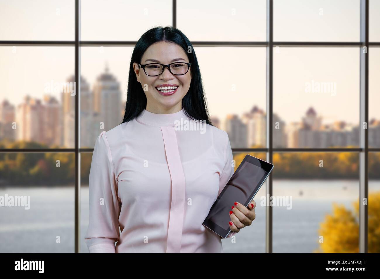 Porträt einer Geschäftsfrau mit Tablet-pc. Karierte Fenster mit Stadtbild im Hintergrund. Stockfoto