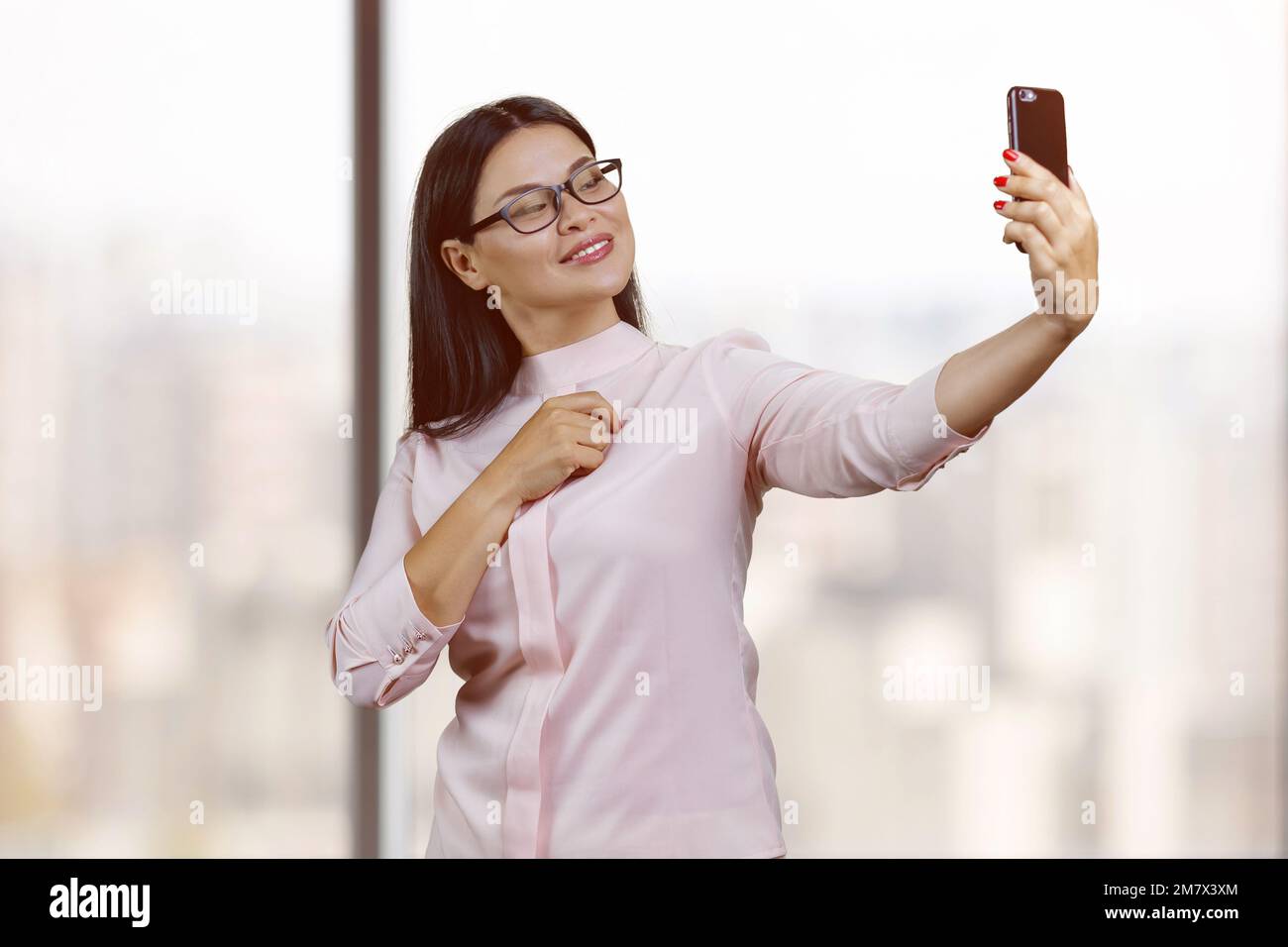 Junge koreanische Geschäftsfrau mit Brille macht ein Selfie. Hintergrund für verschwommene Fenster. Stockfoto