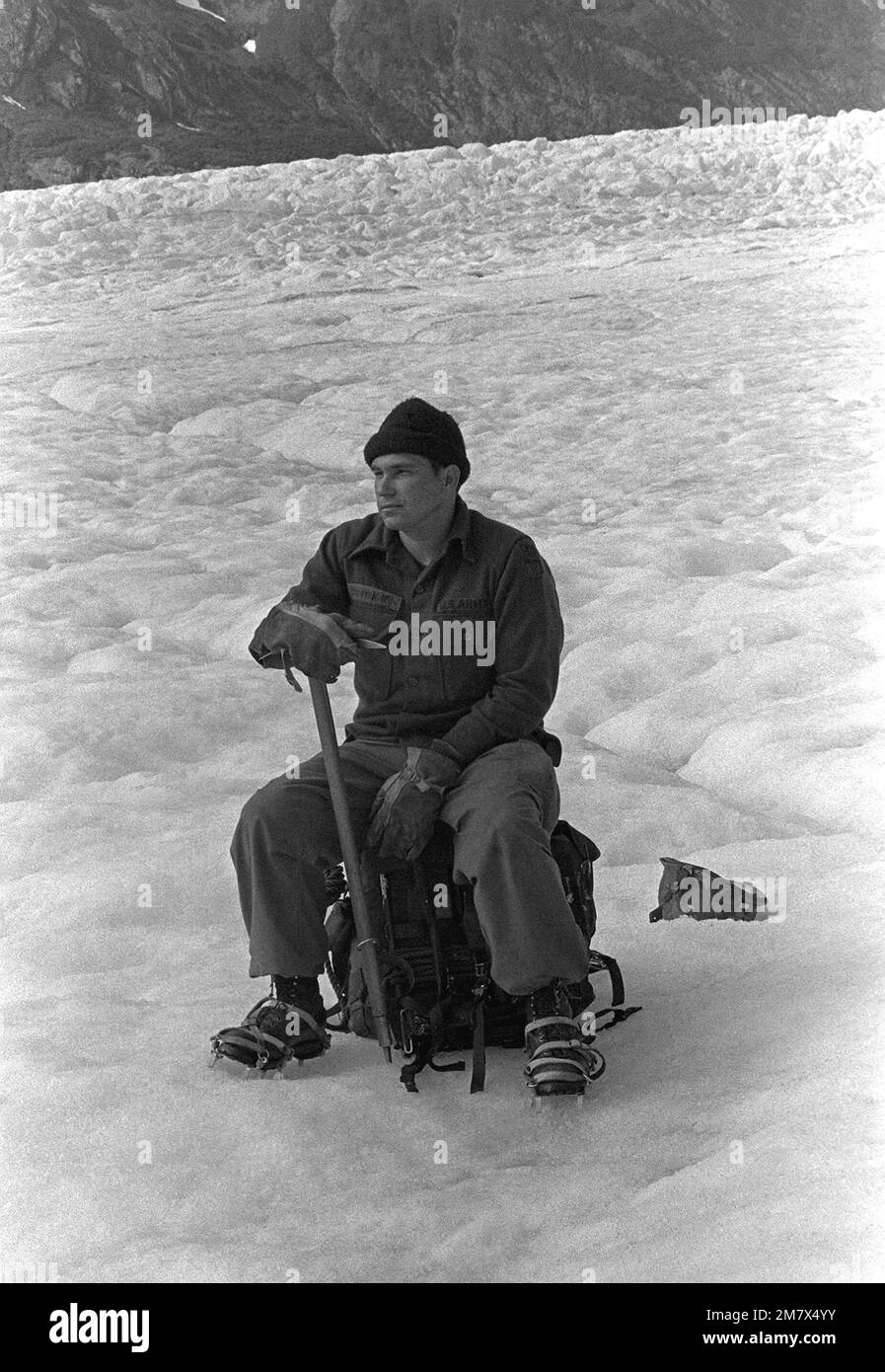 SSGT Glenn Courtwright, 4. Regiment, 23. Infanteriedivision, sitzt auf seinem Rudel und wartet darauf, vom Sheridan Glacier abgeholt zu werden. Courtwright trägt immer noch Eisschuhe und lehnt sich auf den Eispickel, den er während des Gletschertrainings verwendet hat. Basis: Cordova Staat: Alaska (AK) Land: Vereinigte Staaten von Amerika (USA) Stockfoto