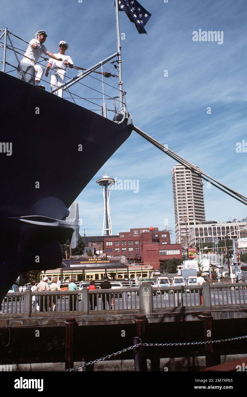 Zwei Crewmitglieder stehen am Steuerbordbug des geführten Raketenkreuzers USS LEAHY (CG-16), im Hafen während der Seemesse 1982. Im Hintergrund ist die Space Needle zu sehen. Basis: Seattle Staat: Washington (WA) Land: Vereinigte Staaten von Amerika (USA) Stockfoto