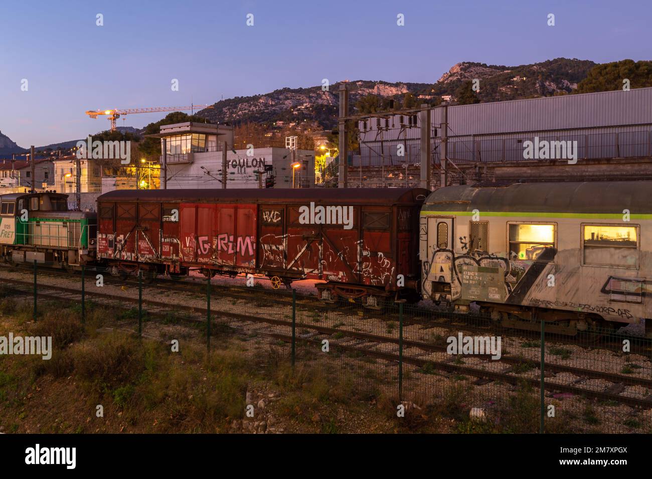 Blick auf die Güterwagen, die in der Abenddämmerung auf den Gleisen am Bahnhof Toulon (Var) geparkt sind. Seit Donnerstag, dem 5. Januar 2023, gilt ein neues Preissystem für den Verkehr, das von der Region Provence-Alpes-Côte d'Azur verwaltet wird. Die Regionalbehörde verwaltet die Zou-Busse und die Regional-Expresszüge (TER), wobei einige Nutzer eine allgemeine Preiserhöhung anprangern. Gleichzeitig kündigt die Region Süd ein umfangreiches Projekt zur Umstrukturierung der Eisenbahn an, mit der Schaffung der neuen PACA-Bahnlinie und einer Erhöhung der Frequenz der TER-Züge (Express Regionaux). Stockfoto