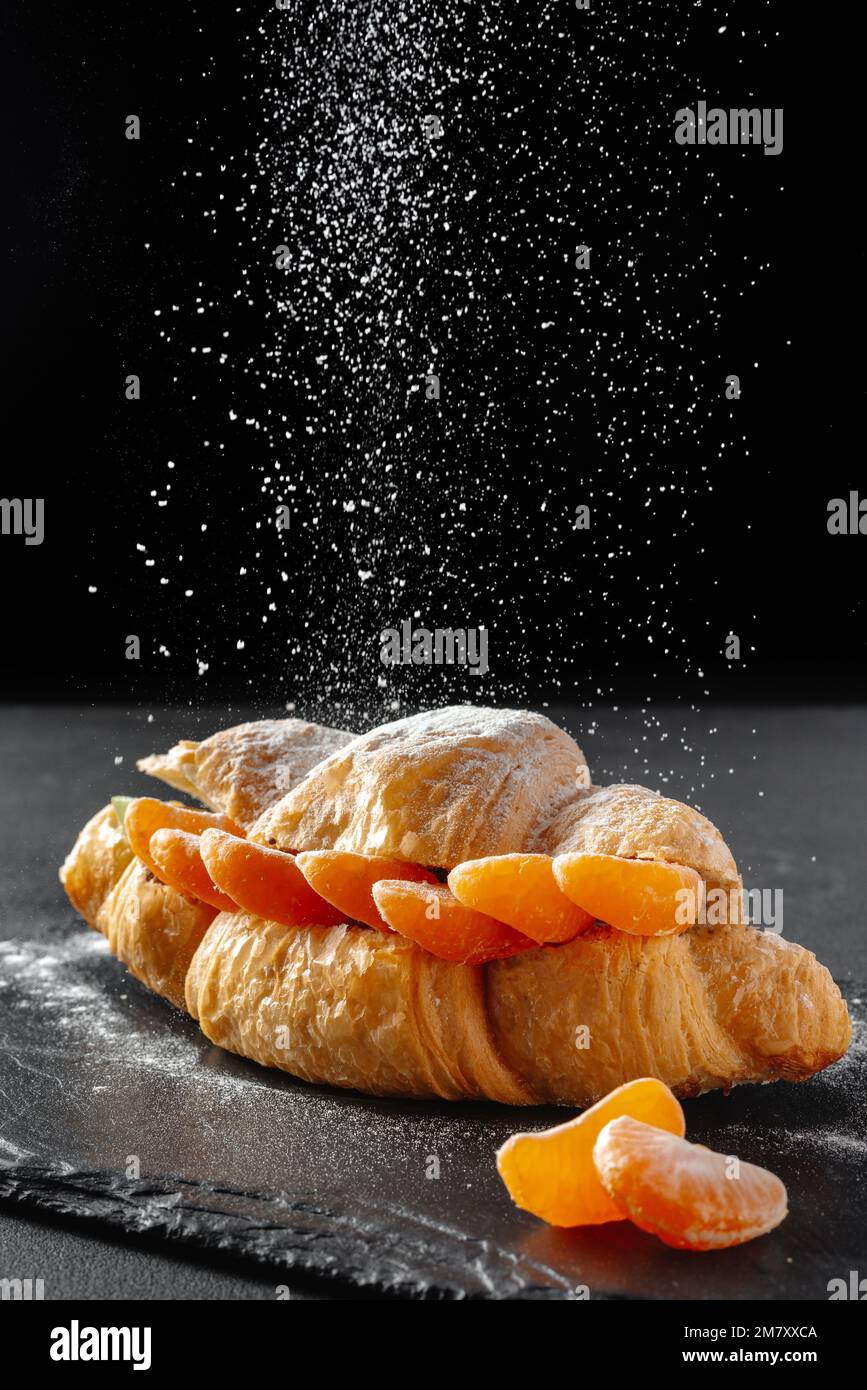 Süßes Croissant-Sandwich mit Puderzucker auf dunklem Hintergrund. Backen- und Bäckereikonzept Stockfoto