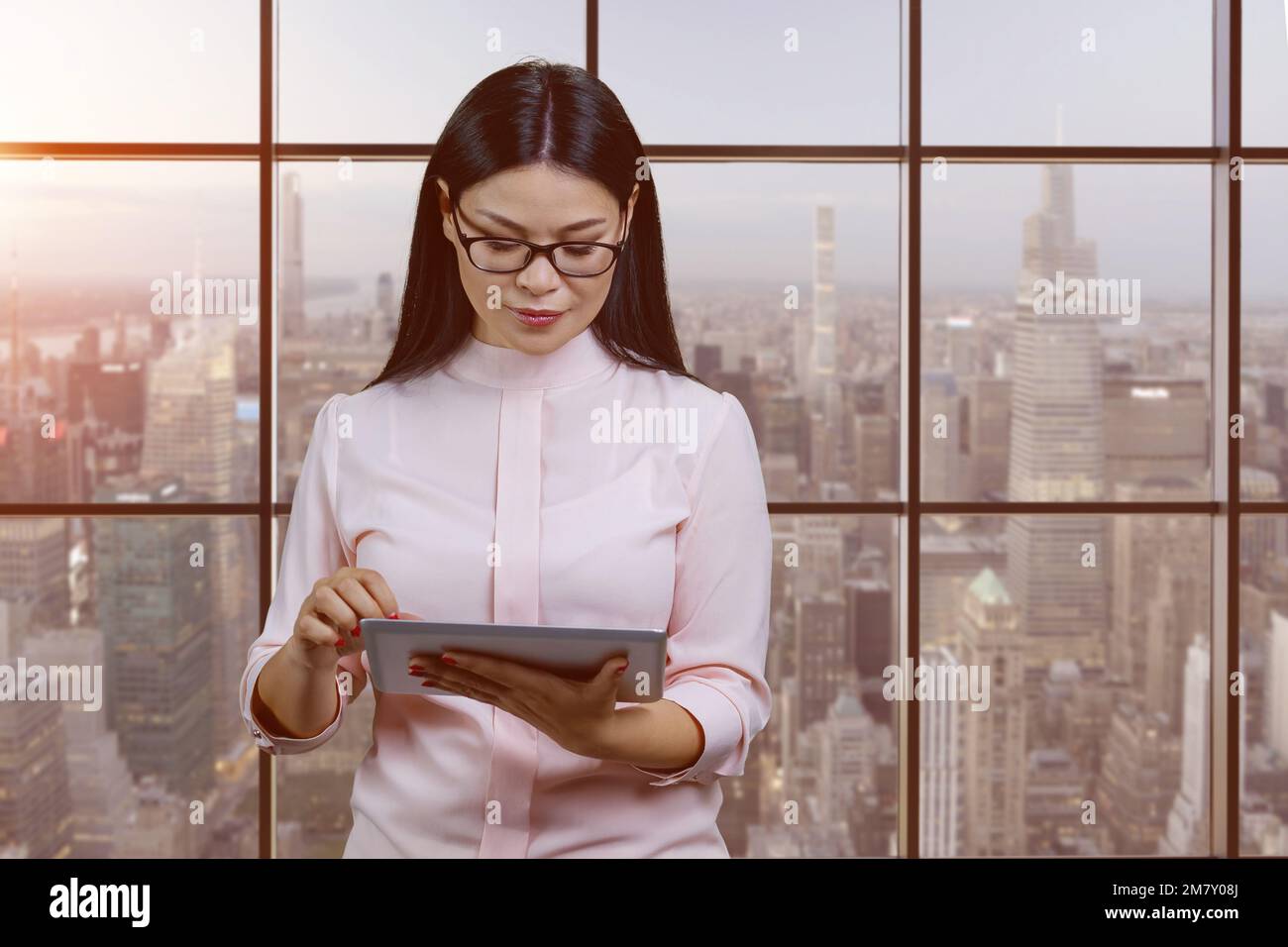 Junge intelligente asiatische Geschäftsfrau, die im Büro einen Tablet-pc verwendet. Fenster und Hintergrund in Großstädten. Stockfoto