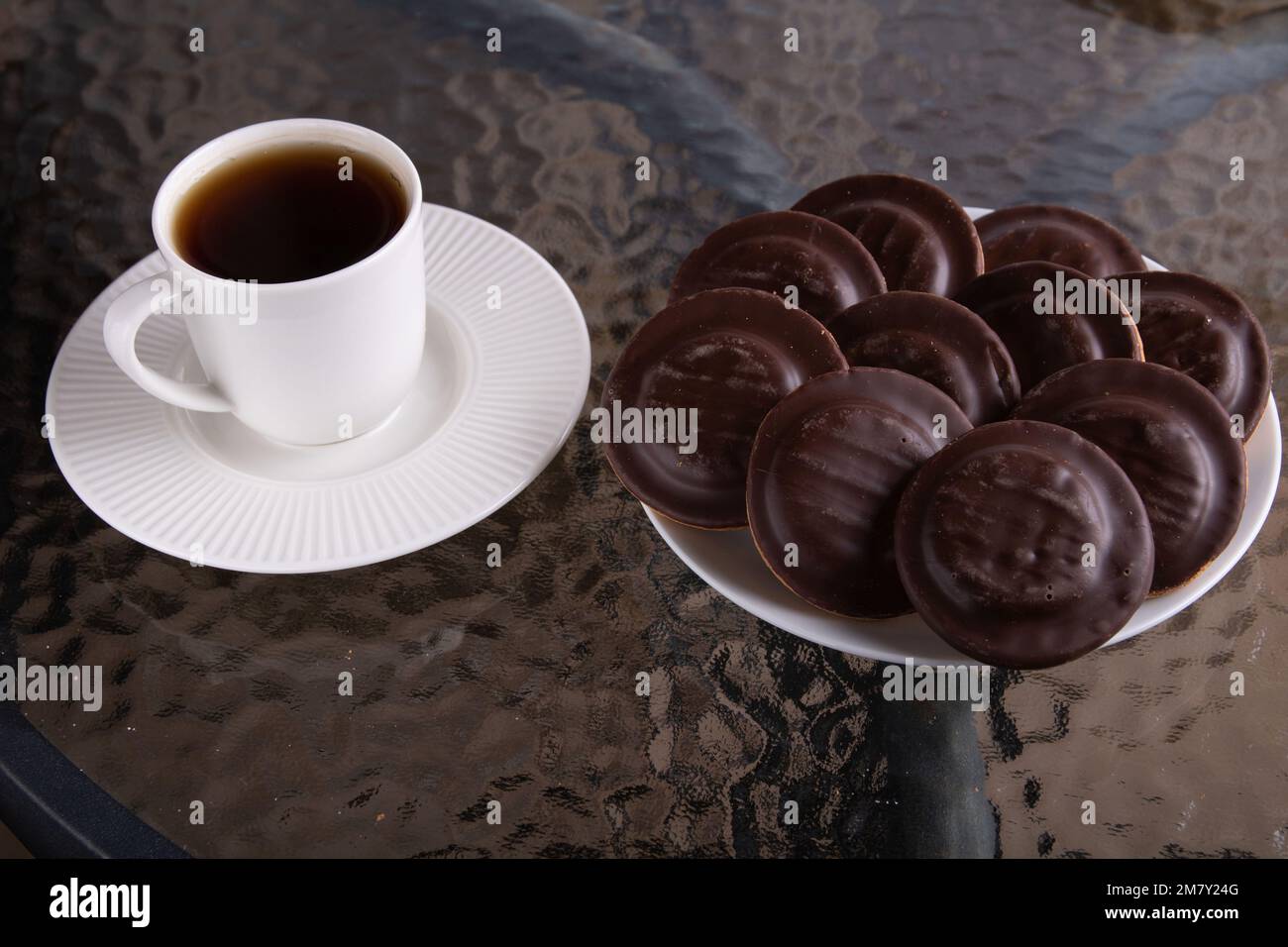 Foto auf einem Glastisch mit einer Tasse Tee auf einer Untertasse und Schokoladenkekse auf einem Teller Stockfoto