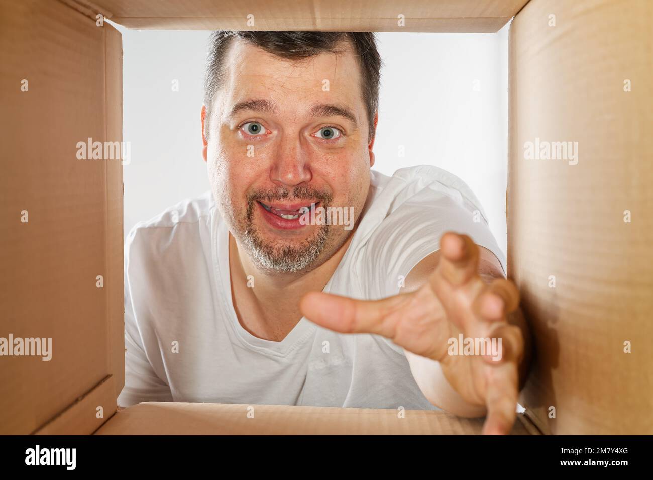 Glücklicher Mann, der auspackt, den Karton öffnet und reinschaut. Ein lächelnder Mann beim Auspacken und eine Schachtel Stockfoto