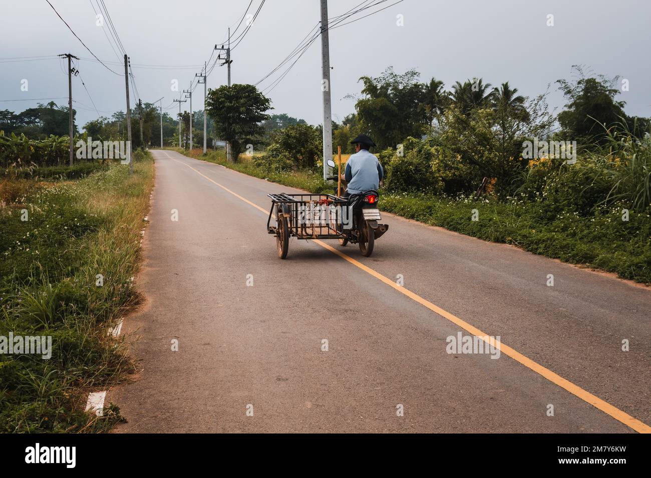 Einheimischer Mann, der auf einem Motorrad mit Seitenwagen auf einer Landstraße in Thailand fährt Stockfoto