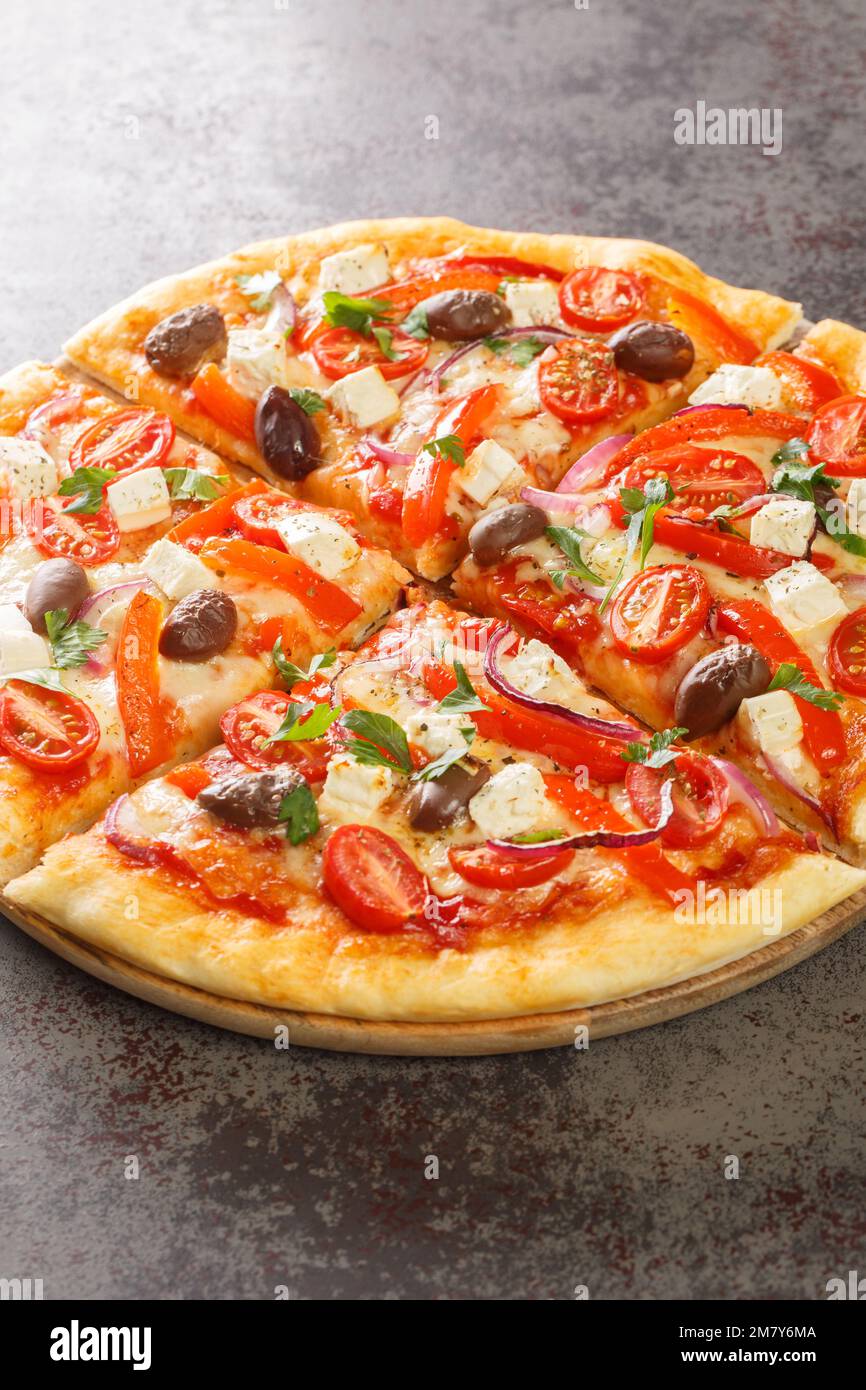 Leckere griechische Pizza auf einer dünnen Teigbasis, die auf dem Holzbrett auf dem Tisch geschnitten wurde. Vertikal Stockfoto