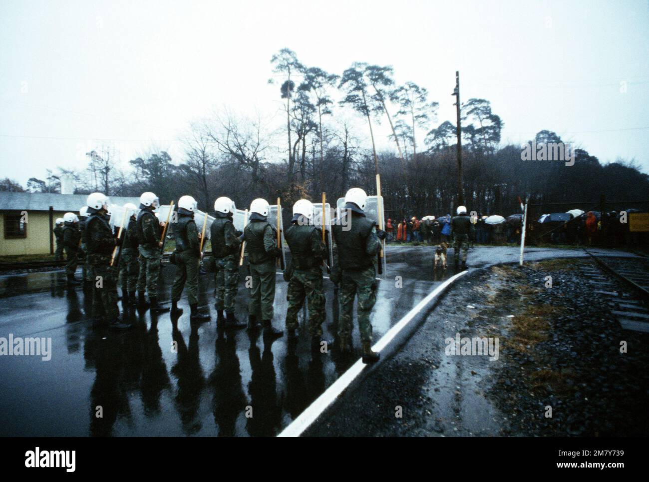 Mitglieder des 435. taktischen Flugzeugflügler-Konfrontations-Management-Teams, in voller Ausrüstung zur Kontrolle von Ausschreitungen, halten sich innerhalb des Umzauns bereit, während Demonstranten vor dem Tor gegen die Entscheidung der NATO demonstrieren, Pershing II und Marschflugkörper in Westeuropa zu stationieren. Basis: Rhein-Main-Luftwaffenstützpunkt Land: Deutschland / Deutschland (DEU) Stockfoto