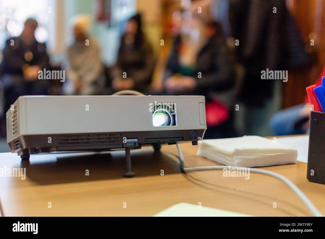 Projektor für Videopräsentationen auf dem Tisch Nahaufnahme des verschwommenen Hintergrunds des Klassenzimmers mit verschwommenen Silhouetten von Personen Stockfoto